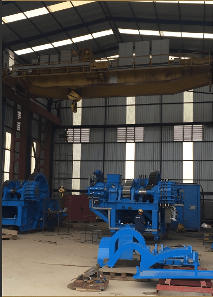 Interior de galpão industrial com equipamentos metálicos de grande porte na cor azul e ponte rolante amarela.