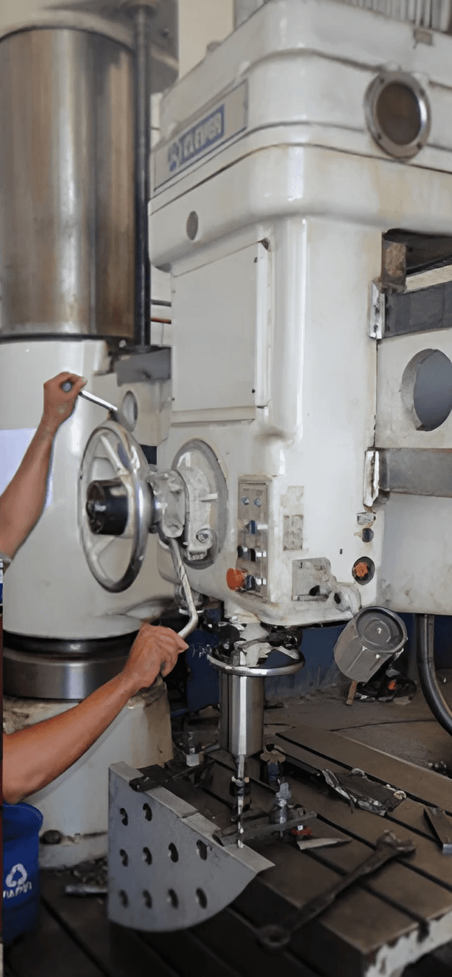 Técnico operando máquina de furação e usinagem de grande porte em oficina industrial.